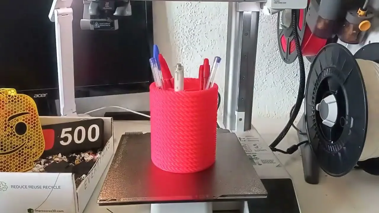 Lapicero rojo con efecto tejido delante de una impresora 3D